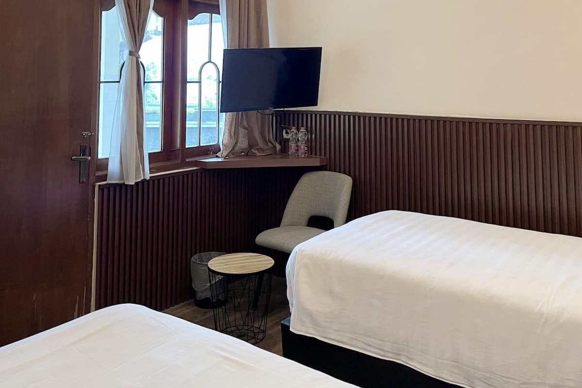 A hotel room with two beds, a TV on a stand, a chair, a small table, and a window with curtains.