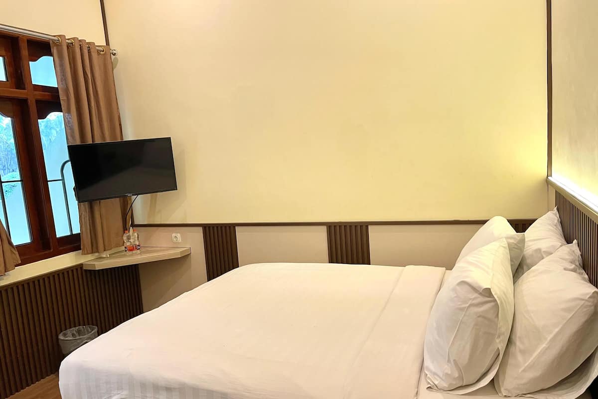 A hotel room with a bed, a TV on a stand, and a window with curtains.