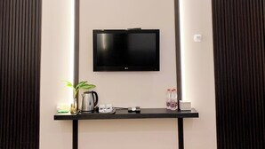 Habitación de hotel moderna con una televisión de pantalla plana montada en la pared, una mesita con una planta, un hervidor de agua, tazas y agua embotellada.