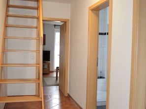 Ein Flur mit einer Holzleiter, einem Fliesenboden und einem Badezimmer mit weißen Fliesen.