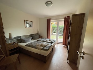 Ein Schlafzimmer mit einem Bett, einem Nachttisch, einer Lampe, einem Sessel und einer Glastür, die auf einen Balkon führt.