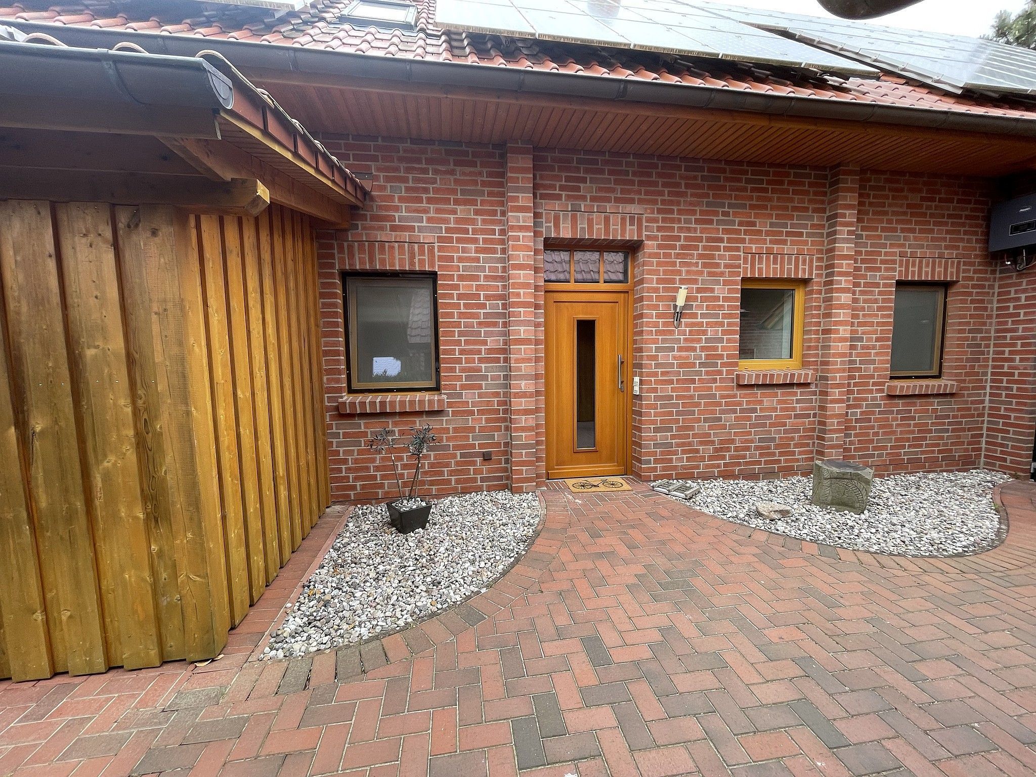 A brick building with a wooden door, two windows, and a small garden area with gravel and plants.