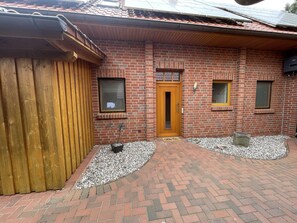 A brick building with a wooden door, two windows, and a small garden area with gravel and plants.