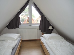 A small, triangular attic bedroom with two beds, a radiator, and a window with curtains. - Suite Dirka 11 OL with balcony (SO) - Usedom Suites 11***, beach 100 m (Karlshagen)