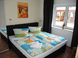 A double bed with a colorful quilt, two pillows, a painting on the wall, and a window with a view of the outside. - Suite Anna with terrace 25 u (SA) - Usedom Suites 25***, beach 100 m (Karlshagen)