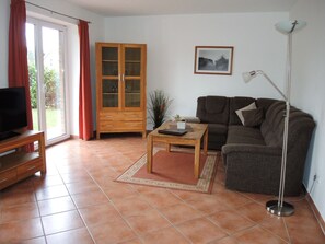 A living room with a sofa, a coffee table, a TV on a stand, a cabinet, and a floor lamp. - Suite Anna with terrace 25 u (SA) - Usedom Suites 25***, beach 100 m (Karlshagen)