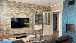 Ein modernes Wohnzimmer mit Steinwand, Flachbildfernseher, einer Vitrine mit Glastüren, einem schwarzen Ledersofa und einer blauen Wand mit Struktur.