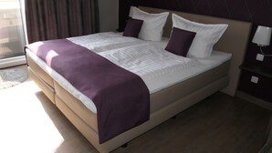 Ein Hotelzimmer mit einem großen Bett, einem Kopfteil mit Rautenmuster, einem Nachttisch mit Lampe und einem Fenster mit Vorhängen.