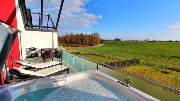 Ein Whirlpool auf einem Balkon mit Blick auf ein grünes Feld und Bäume.