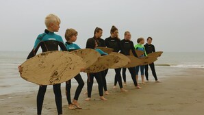 Un grupo de personas con trajes de neopreno sostienen tablas de surf en una playa.