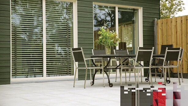 Un patio con una mesa y sillas, una valla de madera, y una casa con ventanas grandes y fachada verde.