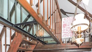 Una escalera de madera con barandilla de vidrio, una lámpara colgante y un tejido estampado cubriendo la barandilla.