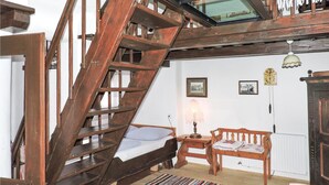 Una habitación rústica con una escalera de madera, una cama, un banco de madera, una lámpara y un reloj de pared.