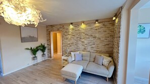 Un salon avec un mur en pierre, un canapé, un pouf, une plante et un lustre.