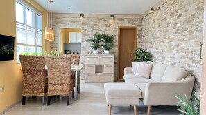 Una sala de estar moderna con sofá, mesa de comedor, sillas de mimbre, zona de cocina y decoración de pared de piedra.
