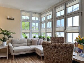 A room with a sofa, wicker chairs, potted plants, and a table with books and a bottle. - Apartment 4 No. - Villa Trautes Heim (Heringsdorf)