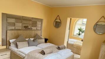 A bedroom with a wooden headboard, a bed with white linens and multiple pillows, a bedside table with a lamp, and a mirror on the wall.