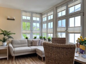 A room with a sofa, wicker chairs, potted plants, and a table with books and a bottle. - Apartment 4 No. - Villa Trautes Heim (Heringsdorf)