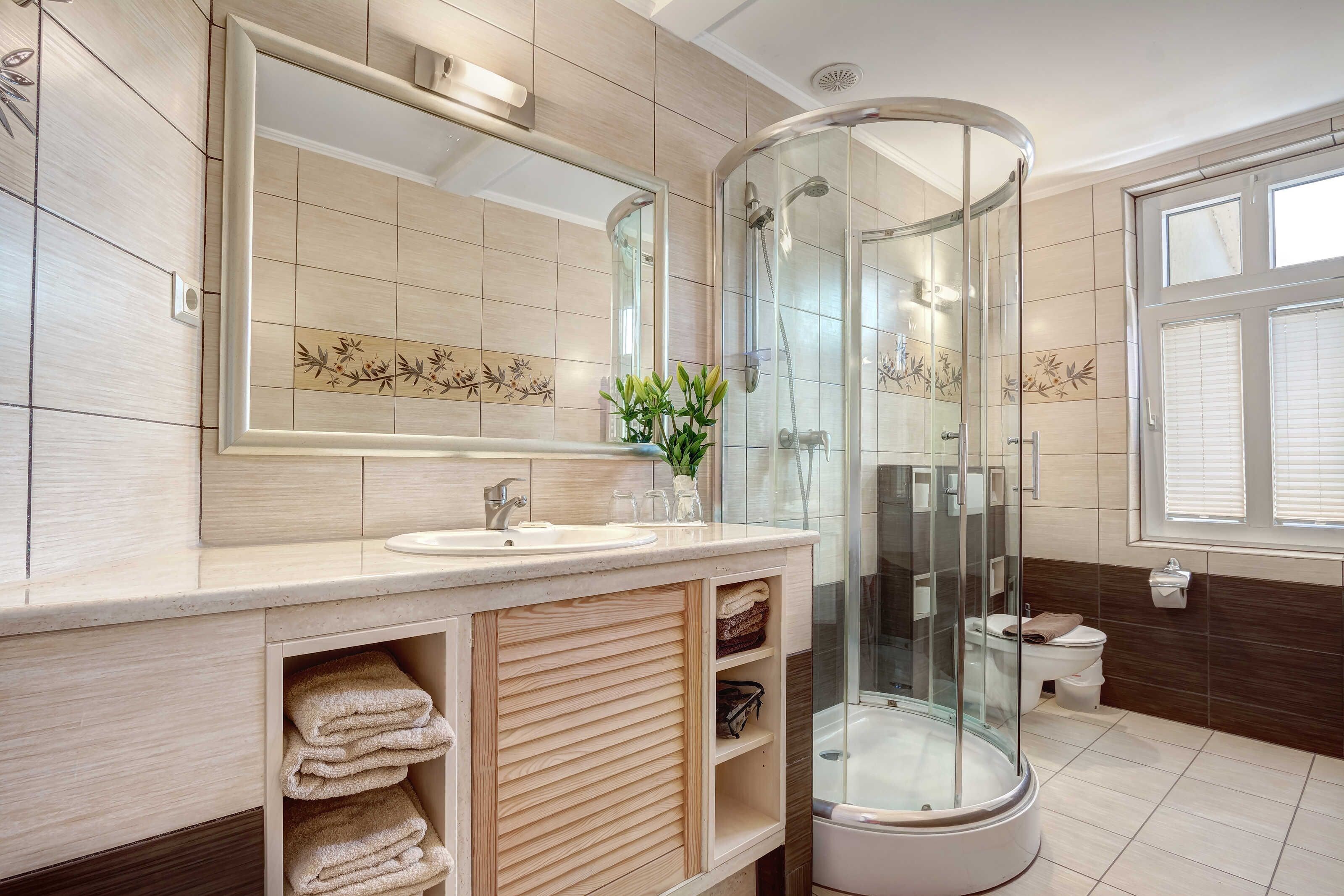 Une salle de bain moderne dotée d’une douche à parois de verre, d’un grand miroir et d’un meuble-lavabo avec un espace pour ranger les serviettes.
