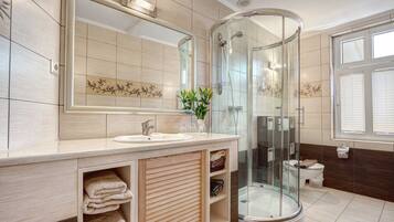 Une salle de bain moderne dotée d’une douche à parois de verre, d’un grand miroir et d’un meuble-lavabo avec un espace pour ranger les serviettes.