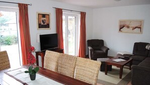 A living room with a wooden dining table, wicker chairs, a sofa, a TV, and curtains. - House 13 Ute (SA) - Usedom Suites House Ute and Baigle***, beach 100 m (Karlshagen)