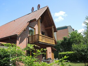 Ein zweistöckiges Haus mit Ziegelaußenwand, einem hölzernen Balkon und einem grünen Rasen.
