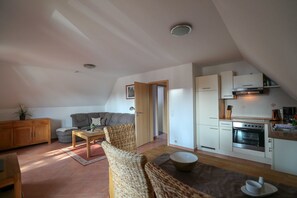 A compact living space with a kitchenette, a sofa, a dining table, and a wicker chair. - Suite Valery with balcony 27 o (SA) - Usedom Suites 27***, beach 100 m (Karlshagen)