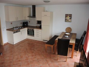A compact kitchen with white cabinets, a stove, and a dining area with a table and chairs. - Suite Valery with balcony 27 o (SA) - Usedom Suites 27***, beach 100 m (Karlshagen)