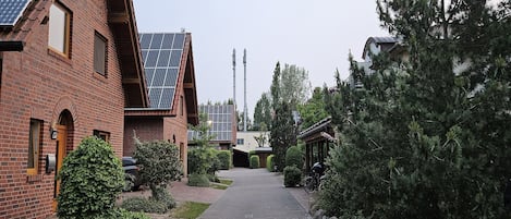 Un edificio de ladrillo con paneles solares, un camino pavimentado y una fila de árboles de hoja perenne.