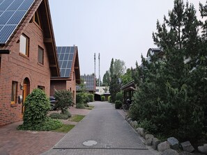 A brick building with solar panels, a paved pathway, and a row of evergreen trees. - Suite Valery with balcony 27 o (SA) - Usedom Suites 27***, beach 100 m (Karlshagen)