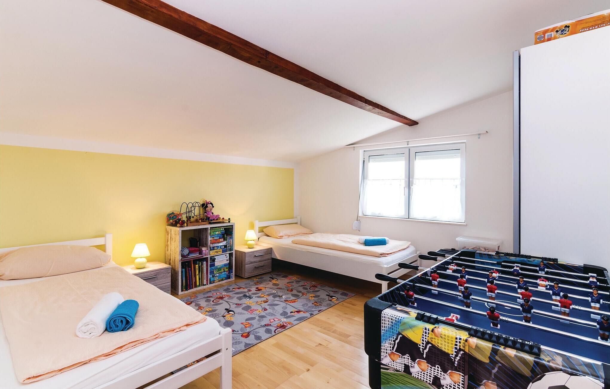 A room with two beds, a foosball table, a bookshelf, and a window.
