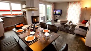 A modern living room with a dining area, a fireplace, a television, and a sofa.