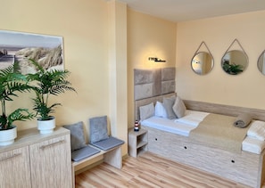 Een slaapkamer met een bed, nachtkastjes, een lamp, een potplant en een spiegel aan de muur.