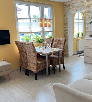 A dining area with wicker chairs, a table with a vase of flowers, and a window with blinds.