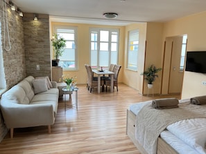 Een moderne woonkamer met een bank, een eettafel met stoelen, een televisie en een bed.