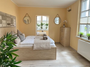 Een slaapkamer met een bed, twee spiegels, een kledingkast en een raam met planten.