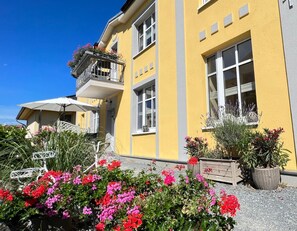 Un bâtiment jaune doté d’un balcon, de fenêtres et d’un jardin fleuri.