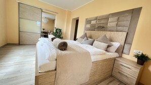 A bedroom with a large bed, a wooden headboard, a bedside table, and a small drawer unit. - Apartment 1 ground floor - Villa Trautes Heim (Heringsdorf)