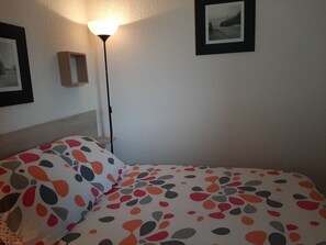 A bedroom with a bed, a nightstand, a lamp, and two framed pictures on the wall. - Renovated apartment on 2nd floor, near the beach in Seignosse (Seignosse)