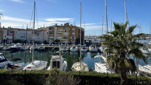 Ein Yachthafen mit mehreren vertäuten Booten, eine Reihe bunter Gebäude im Hintergrund und eine Palme im Vordergrund.