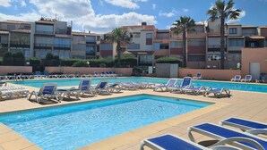 Ein Swimmingpool mit Liegestühlen, umgeben von mehrstöckigen Gebäuden mit Balkonen und Palmen.