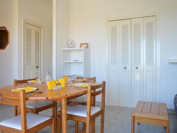 A dining area with a wooden table and chairs, a small wooden bench, and a white door with louvered shutters.