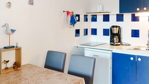 Et lille køkken med kaffemaskine, minikøleskab og spiseplads med to stole.