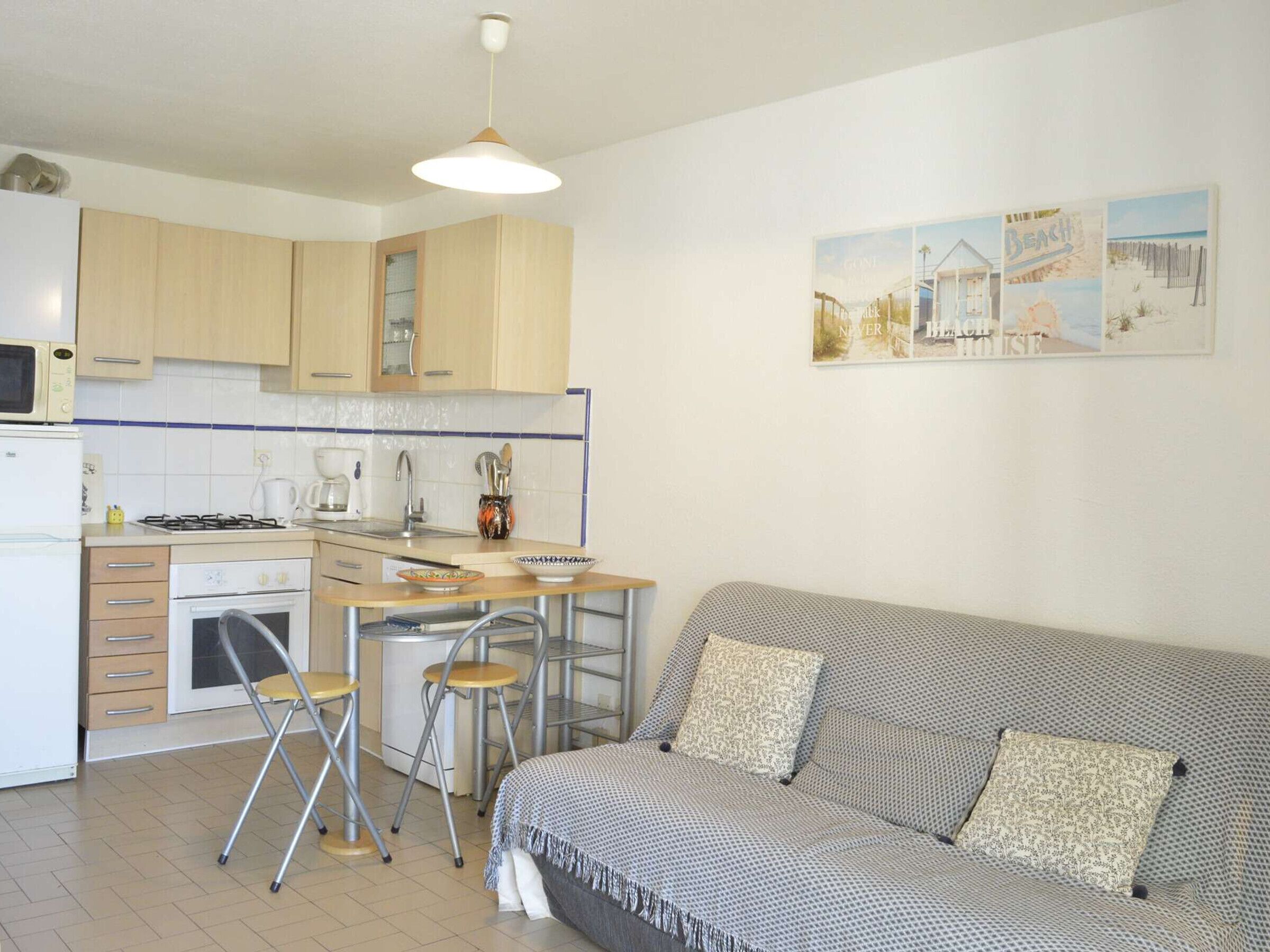 A compact kitchen with a dining area, a sofa, and a wall with beach-themed artwork.