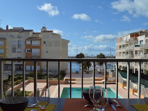 Un balcón con vistas a un puerto deportivo, una piscina y edificios residenciales cercanos.