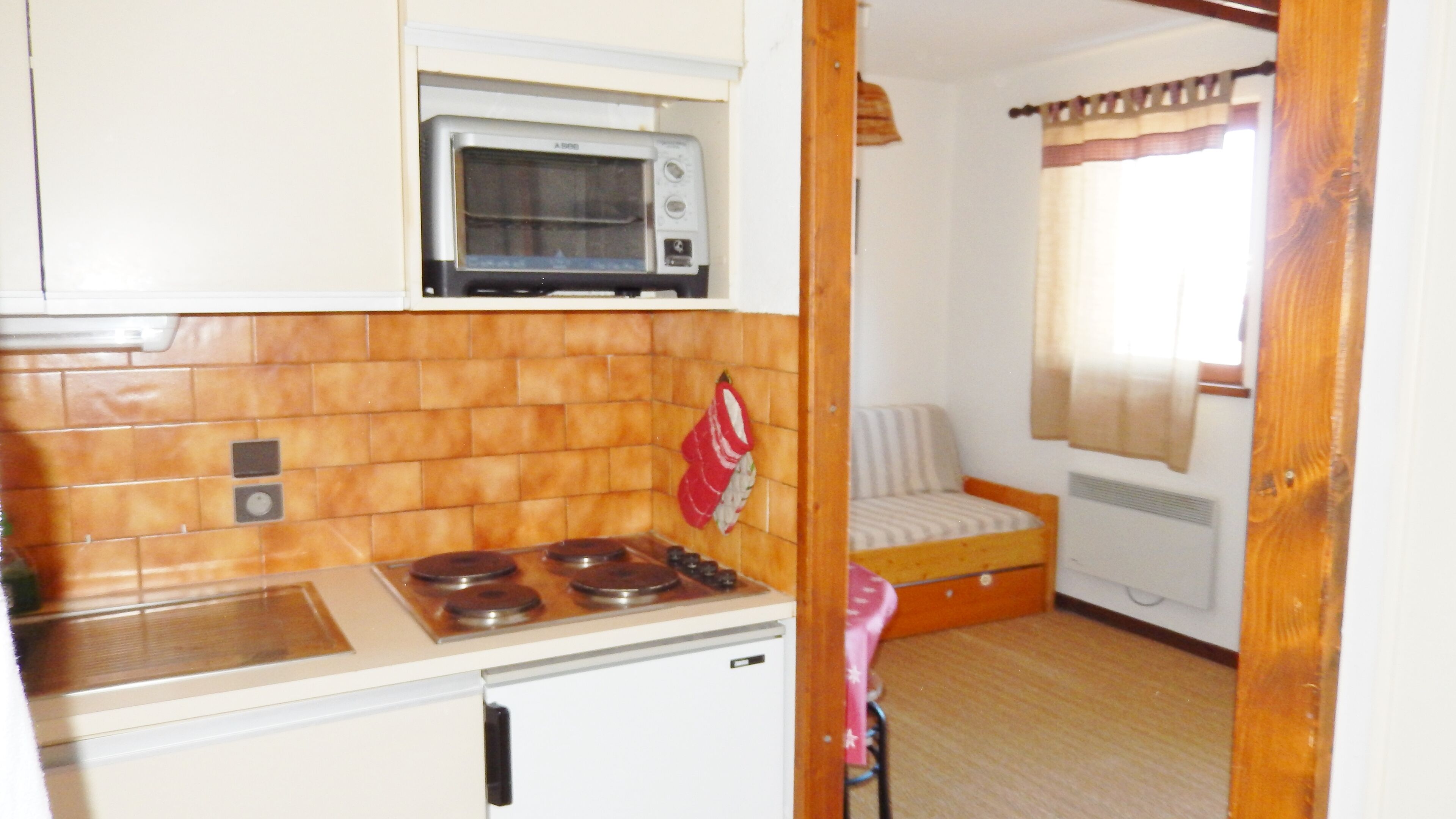 Cocina compacta con estufa, horno y microondas. Cuenta con un pequeño comedor con una silla y un radiador.