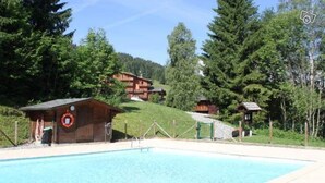 A swimming pool with wooden cabins in a forested area.