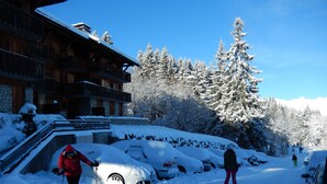 A wooden lodge with a balcony, surrounded by snow-covered trees and a clear sky.