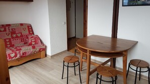 A cozy room with a wooden dining table, four stools, a patterned sofa, and a wooden cabinet.