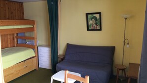 Una habitación con literas, una cama individual, un escritorio, una silla, una lámpara y un cuadro en la pared.